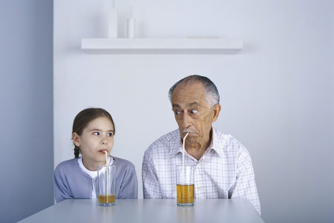 Un grand-père et sa petite-fille attablés, buvant une boisson à la paille en se regardant